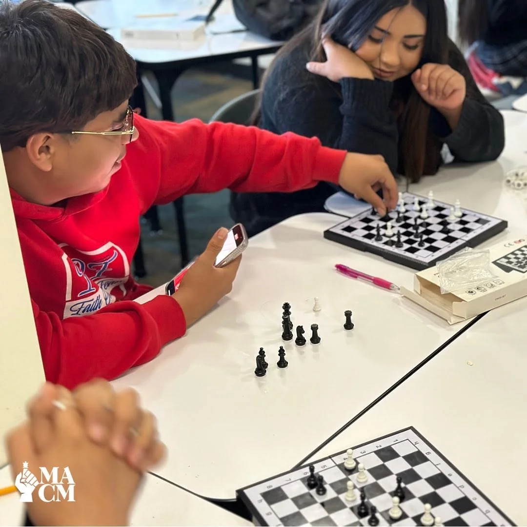 A close-up of a youth in a red hoodie reaching toward a chessboard